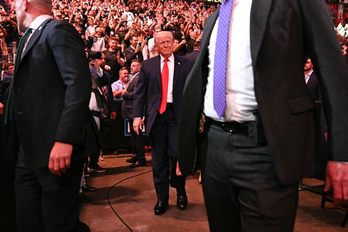 Several formally dressed individuals, including a man in a red tie, are walking through a crowded venue.