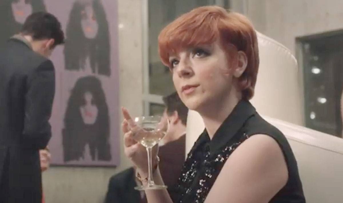 A woman holds a cocktail glass and looks serious