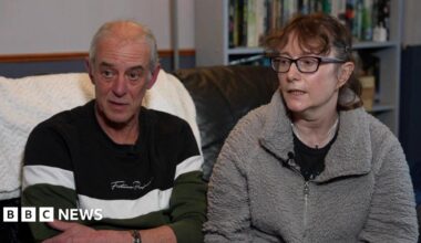 Ken and Kerstin Rudd. Ken is wearing a blue and white striped jumper and has short grey hair. Kerstin is wearing a fluffy grey top over a black t shirt and has glasses and short brown hair. Both are seated on a sofa.