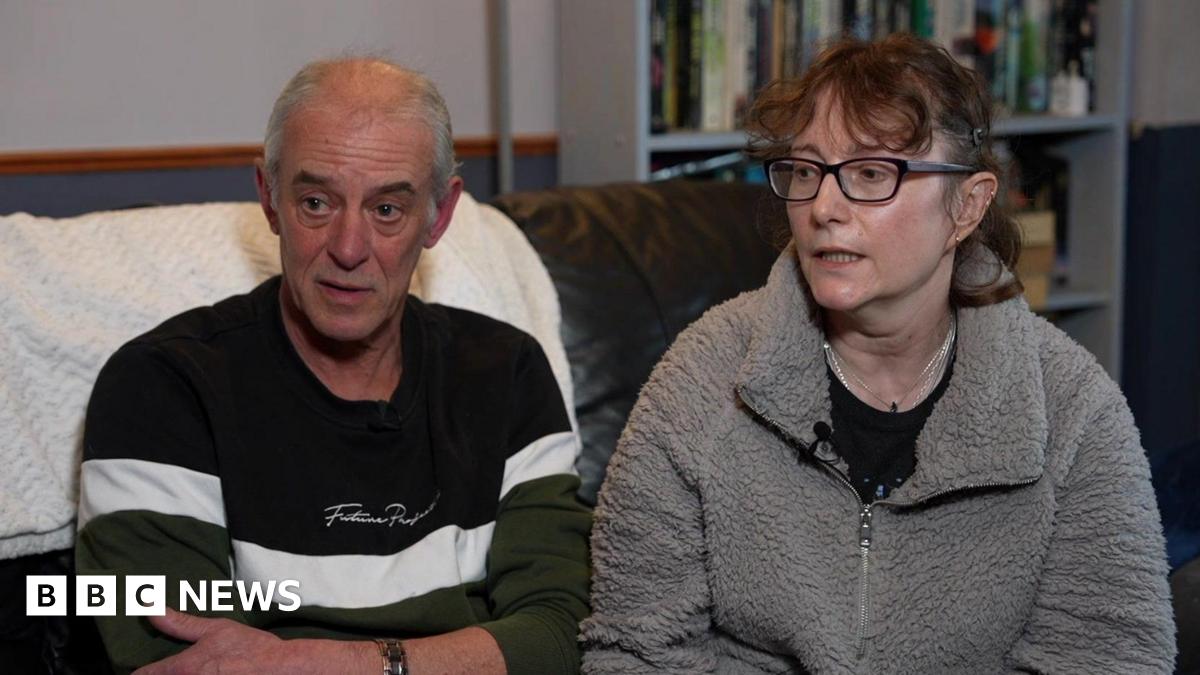 Ken and Kerstin Rudd. Ken is wearing a blue and white striped jumper and has short grey hair. Kerstin is wearing a fluffy grey top over a black t shirt and has glasses and short brown hair. Both are seated on a sofa.