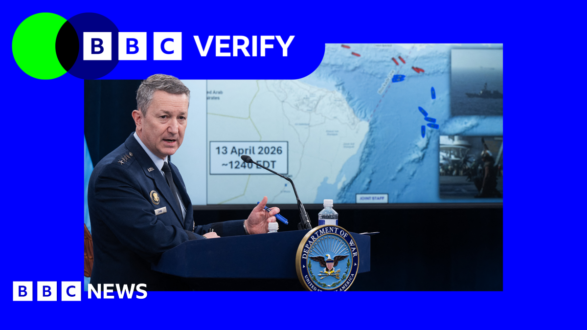 Gen Dan McCaine wearing a blue US Air Force uniform stands at a lectern in front of a screen showing a map of the Strait of Hormuz and the Gulf of Oman