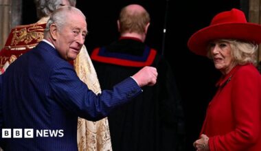 The King and Queen turn around to look behind them. The King holds a hand up while the Queen smiles