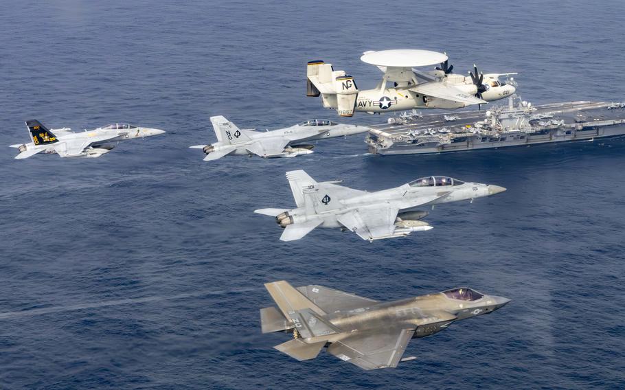 Five aircraft fly over a large military ship.