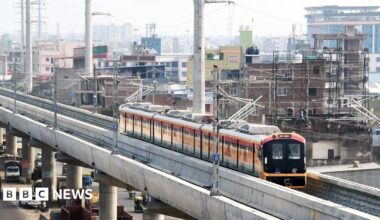 Two young men and a woman who is between them, take a selfie while traveling on the Aqua Line metro train in Mumbai.