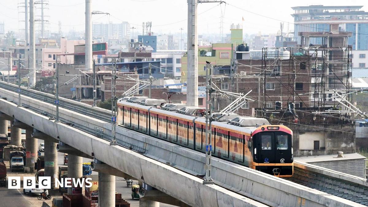 Two young men and a woman who is between them, take a selfie while traveling on the Aqua Line metro train in Mumbai.