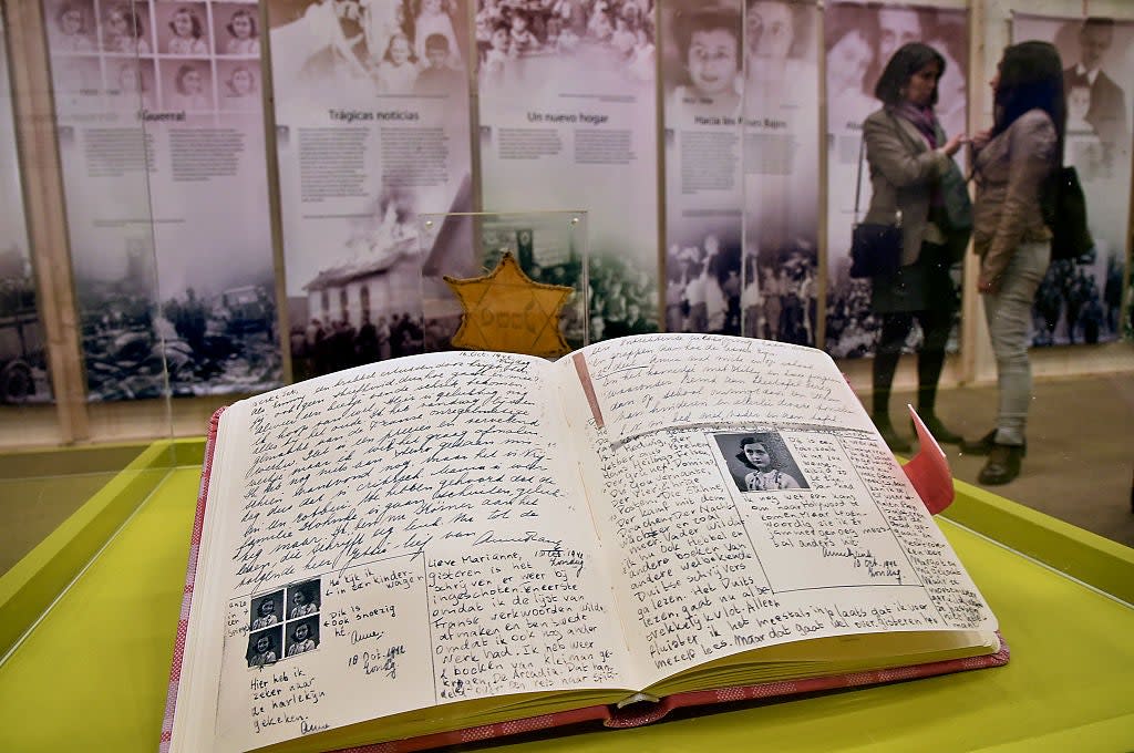 Open diary with handwritten notes and photos displayed in a museum setting, with two visitors chatting in the background