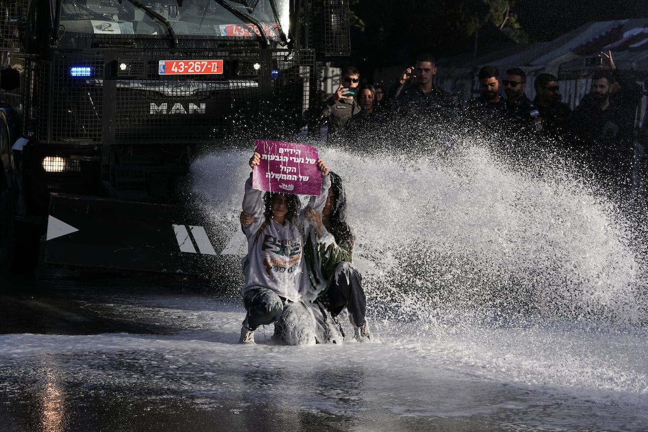 Two individuals hold a sign while being sprayed with water.