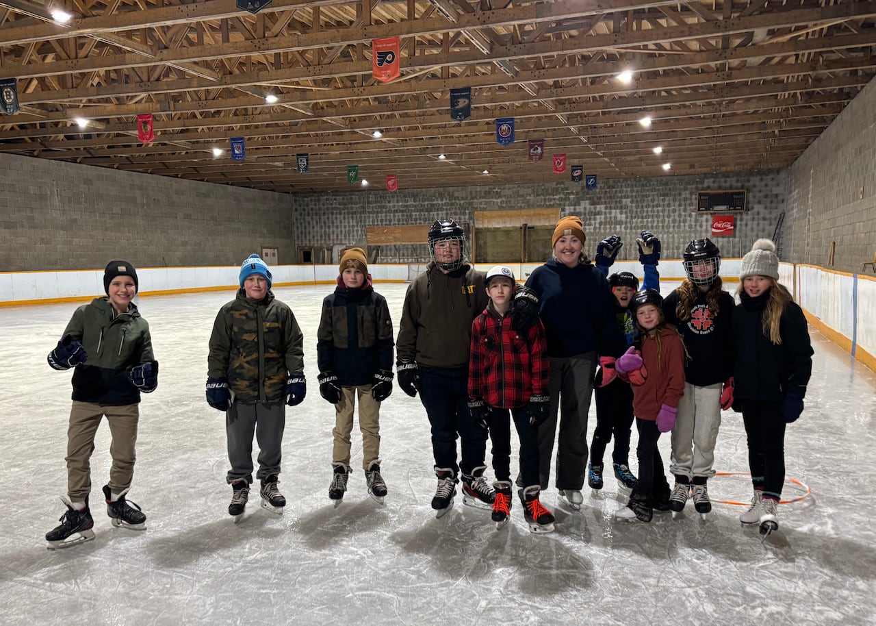 Children and adults in skates pose on the ice inside a hockey rink.