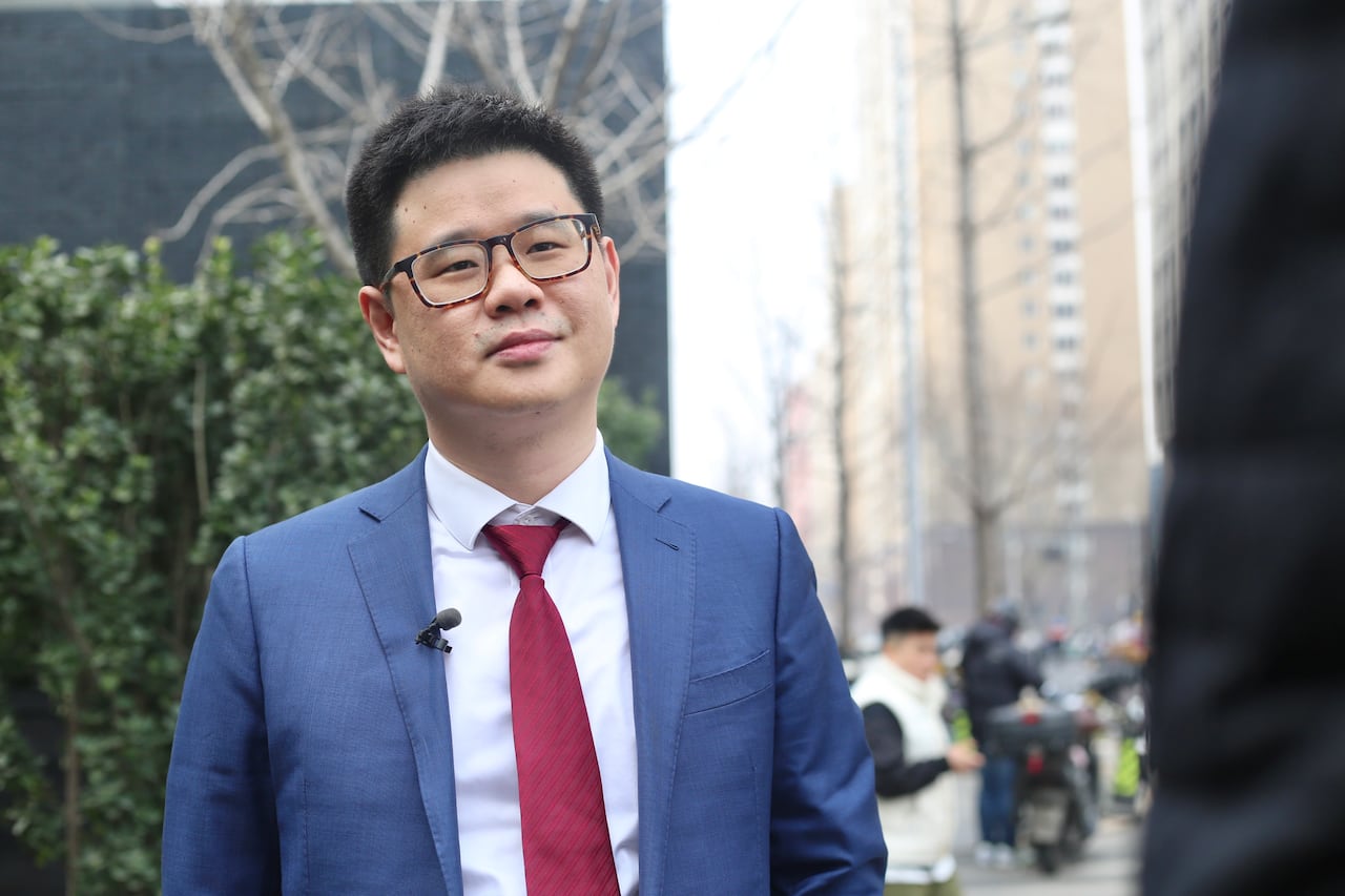 A man in a blue suit and red tie stands outside. 