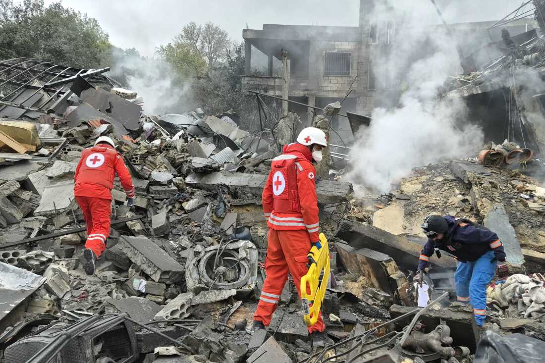 Three first aid responders wearing arrive at the site of an Israeli airstrike that demolished buildings in Kfar Roummane on March 26.