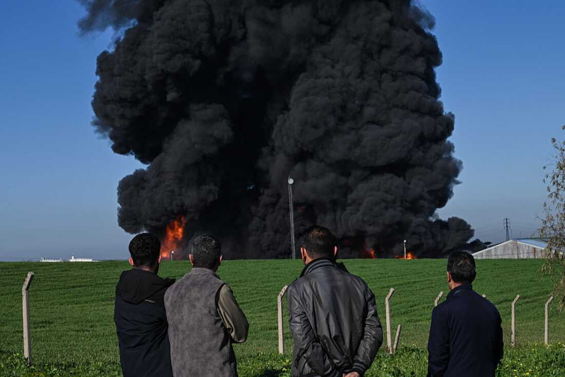 People watch as smoke billows from an oil warehouse in the Kani Qirzhala area on the outskirts of Erbil, the capital of Iraq's autonomous Kurdistan region, following a suspected drone strike, on April 1, 2026.