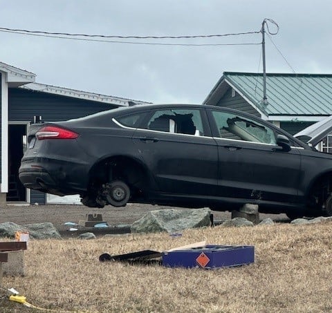 A photo shows a black vehicle with broken windows and its tires removed.