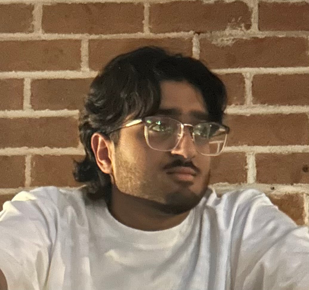 Man wearing white t-shirt and glasses looking to the side in front of a brick wall. 