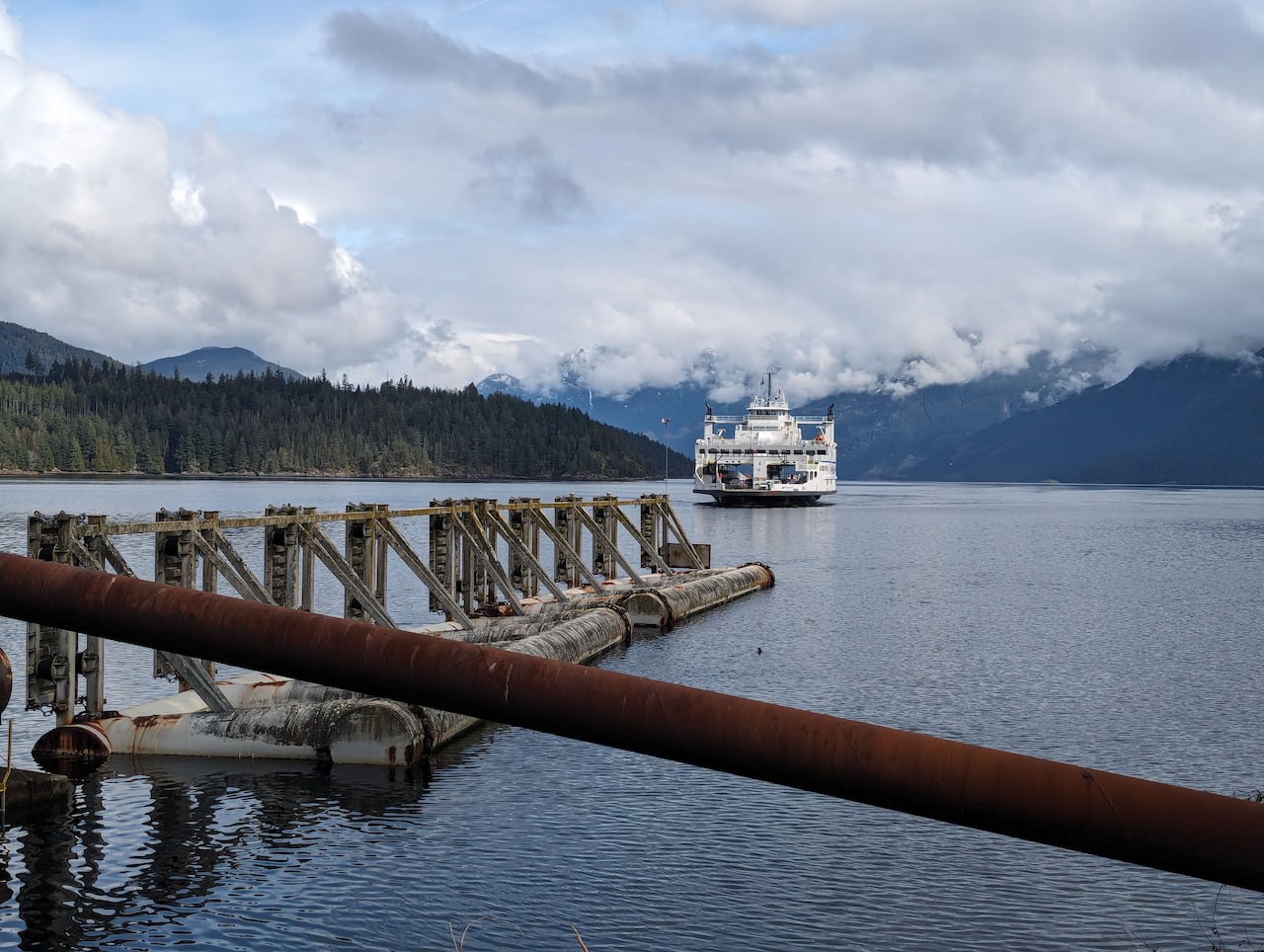 A large white boat is approaching a doc. In the background there are large snow-capped mountains
