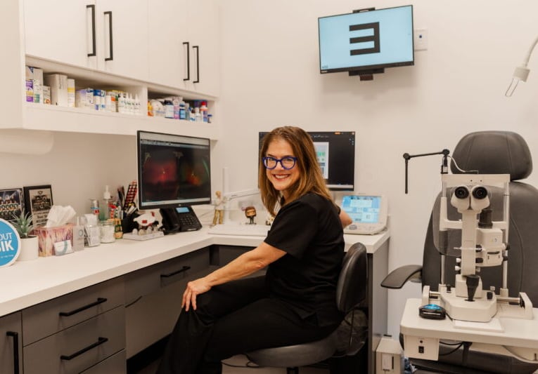 A woman sits in a chair at her desk within an optometrist's office