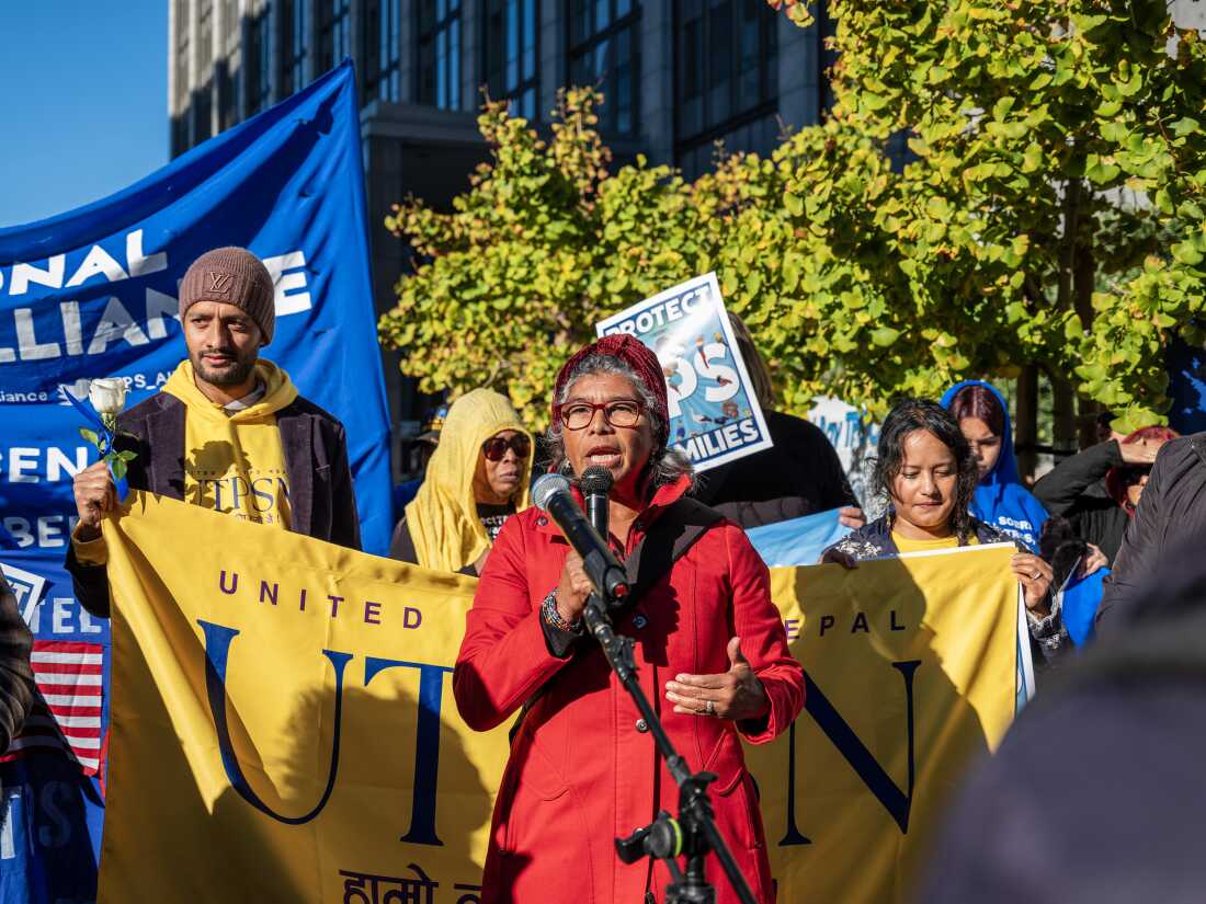 Rosa María Carranza holds a microphone and others hold signs at a protest outside a courthouse.