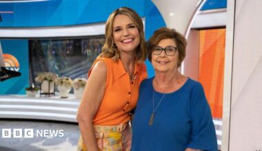 Savannah Guthrie and mother Nancy Guthrie on the Today show set in June 2023. Savannah has long light brown hair and is wearing an orange sleeveless shirt and colourful floral trousers. Nancy has short brown hair and is wearing a blue top with a long necklace