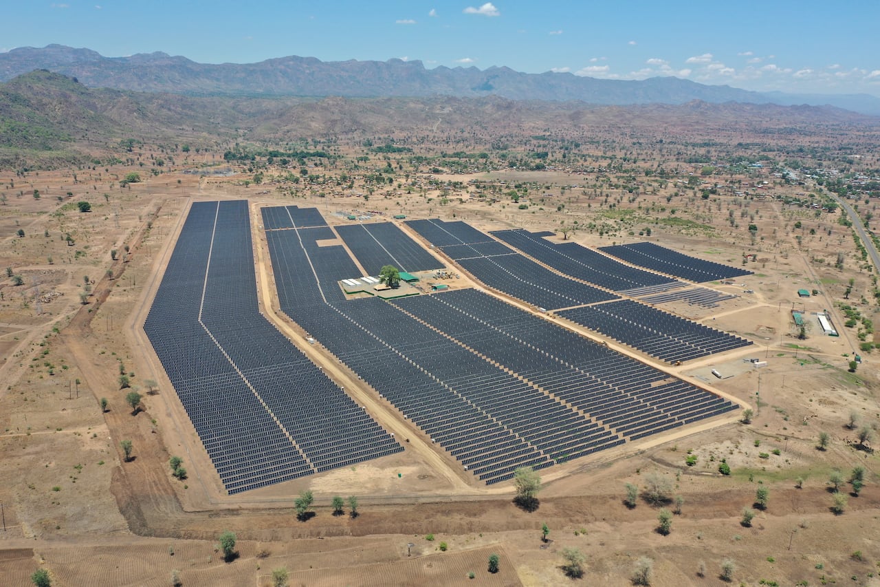 Aerial view of solar farm surrounded by scrubland with mountains in the background