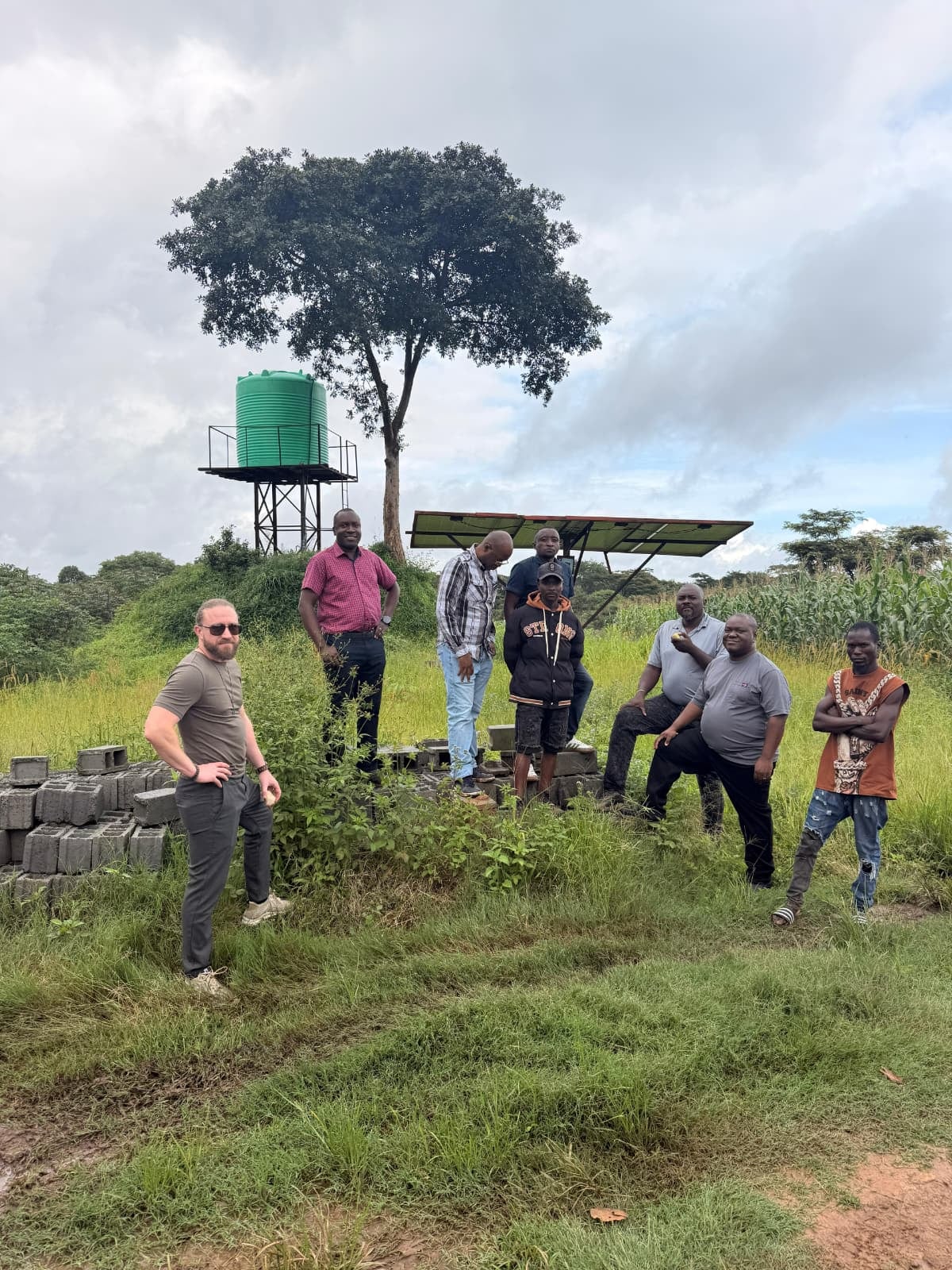 Eight people standing on the grass in front of a water tank, a tree and a solar panel