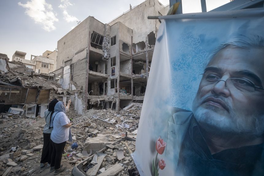 Two Iranian women stand next to a banner featuring a portrait of Iranian nuclear scientist Mohammad Mehdi Tehranchi, who was killed in Israeli attacks.