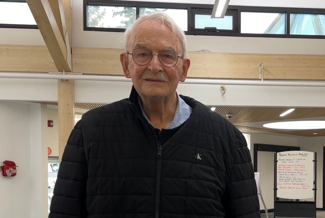 An older man in a black coat holds a cane.