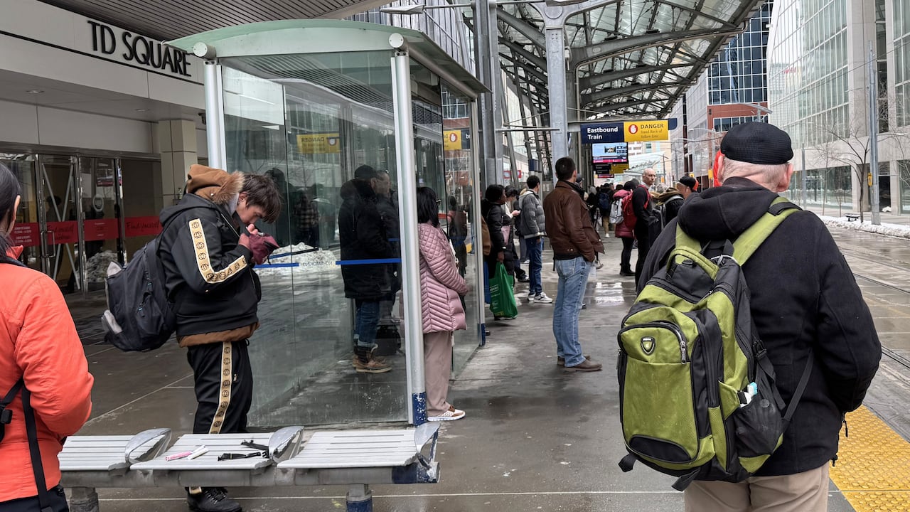 A man smokes a substance on a train platform about two metres from other transit passengers.