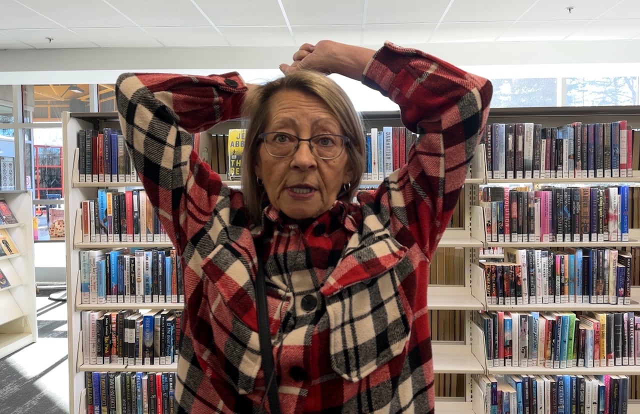 A woman in a plaid shirt at a library holding her hands above her head.