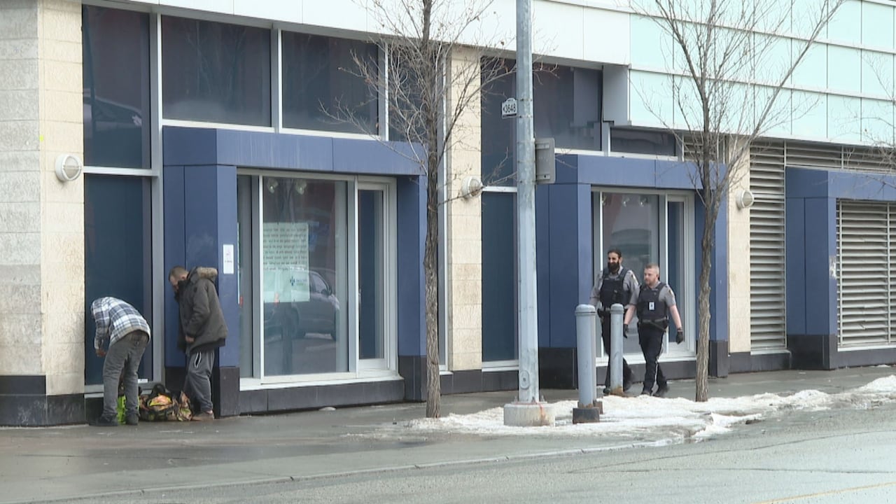 Two security walk up to two men standing on a corner and going through shopping bags.