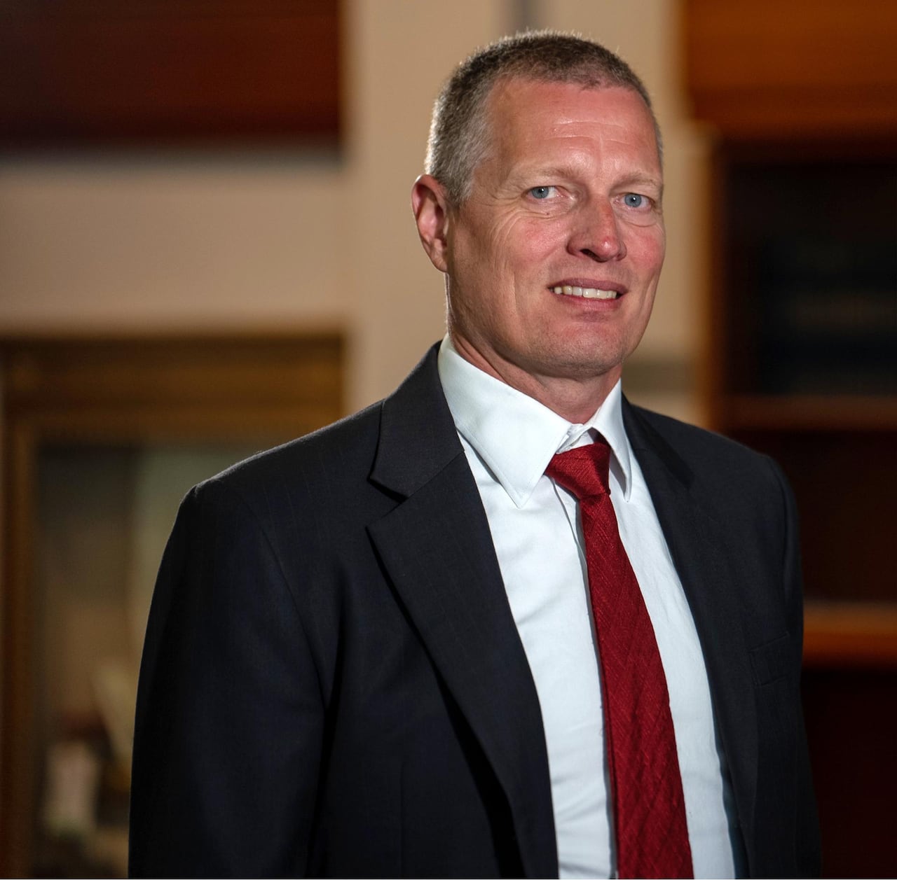 A man in a suit is smiling at the camera. He has close-cropped hair.