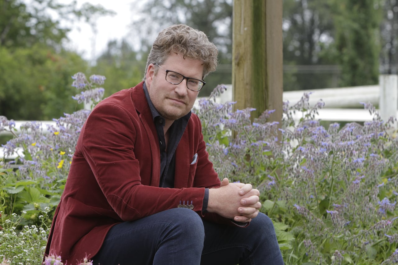 A man in a burgundy sport coat poses for a portrait in front of a flower bed featuring purple blooms.