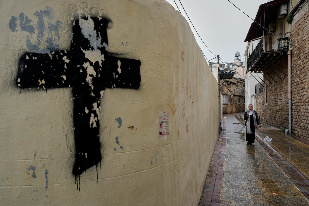 A woman walks down an alleyway. A wall is painted with a black cross.