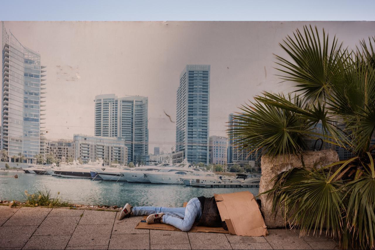 A displaced man sleeps on a street next to a billboard showing Beirut's Marina on April 6, 2026. (AFP Photo)