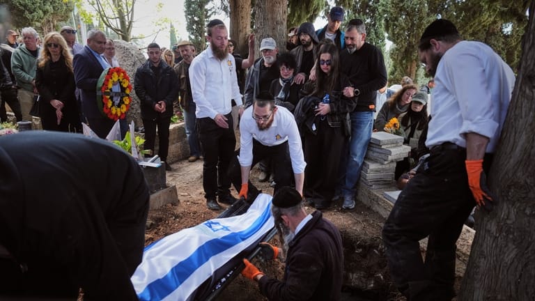 Mourners carry the flag-draped bodies of three members of the...