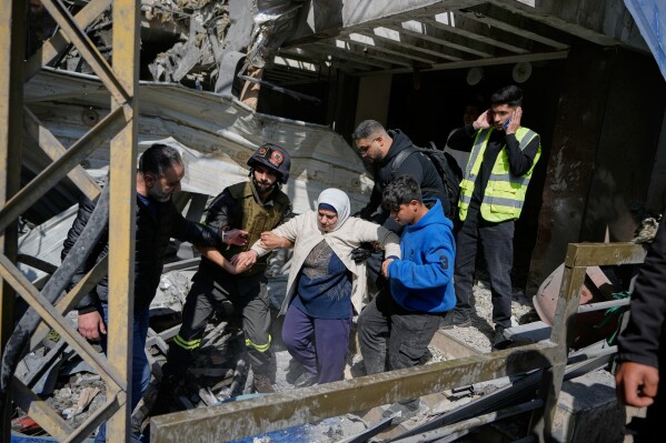 A woman is assisted to leave a destroyed building at the site of an Israeli airstrike that struck an apartment building in Beirut, Lebanon, Wednesday, April 8, 2026. (AP Photo/Bilal Hussein)