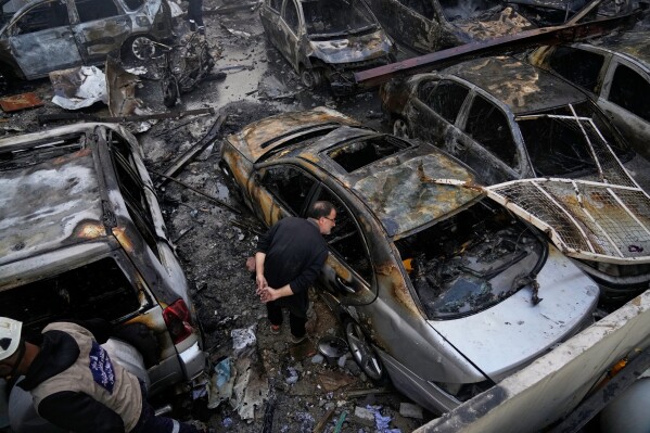 A man peers inside a burned car at the site of an Israeli airstrike that struck a building in Beirut, Lebanon, Wednesday, April 8, 2026. (AP Photo/Hassan Ammar)