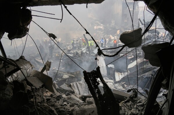Firefighters, volunteers and first responders walk on smoldering debris at the site of an Israeli airstrike that struck a building in Beirut, Lebanon, Wednesday, April 8, 2026. (AP Photo/Hassan Ammar)