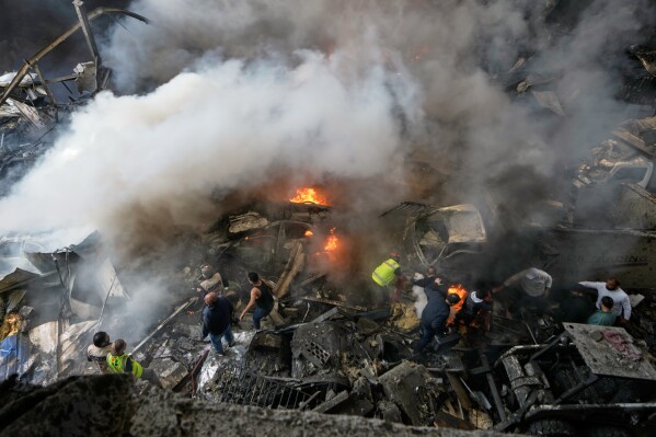 First responders and volunteers search through the rubble beside burning cars at the site of an Israeli airstrike that struck an apartment building in Beirut, Lebanon, Wednesday, April 8, 2026. (AP Photo/Bilal Hussein)