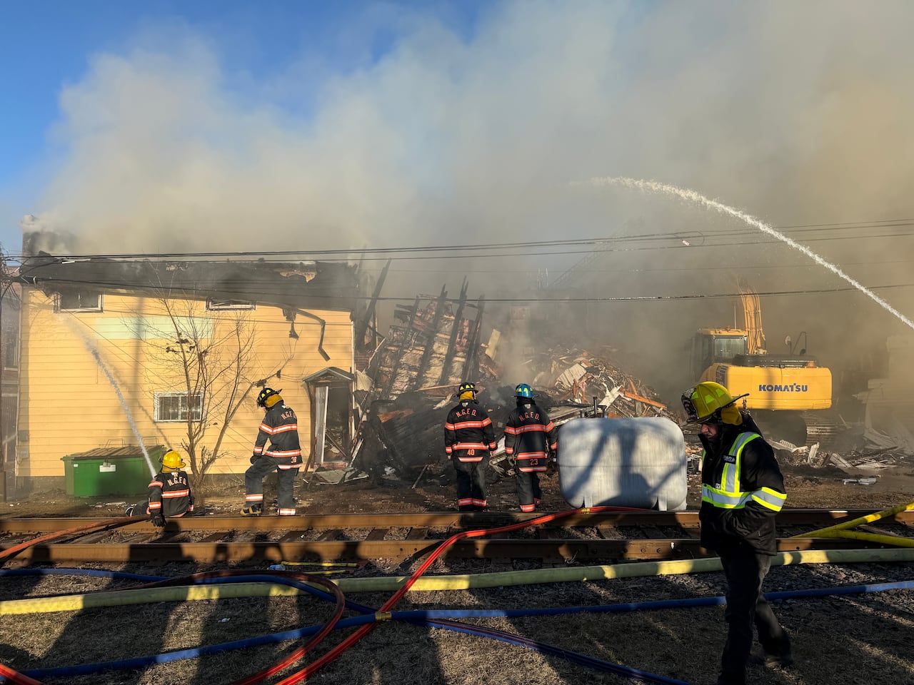 a burnt building with fire fighters in front of it and an exvacator