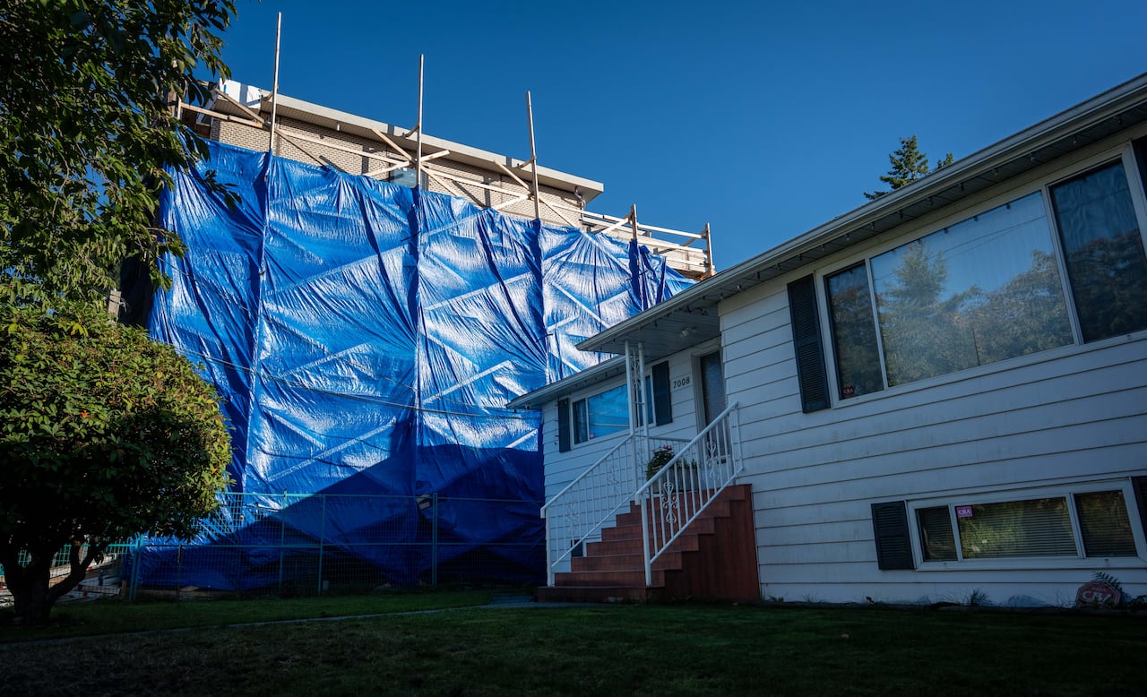 Blue construction tarp is seen next to a single-family home.