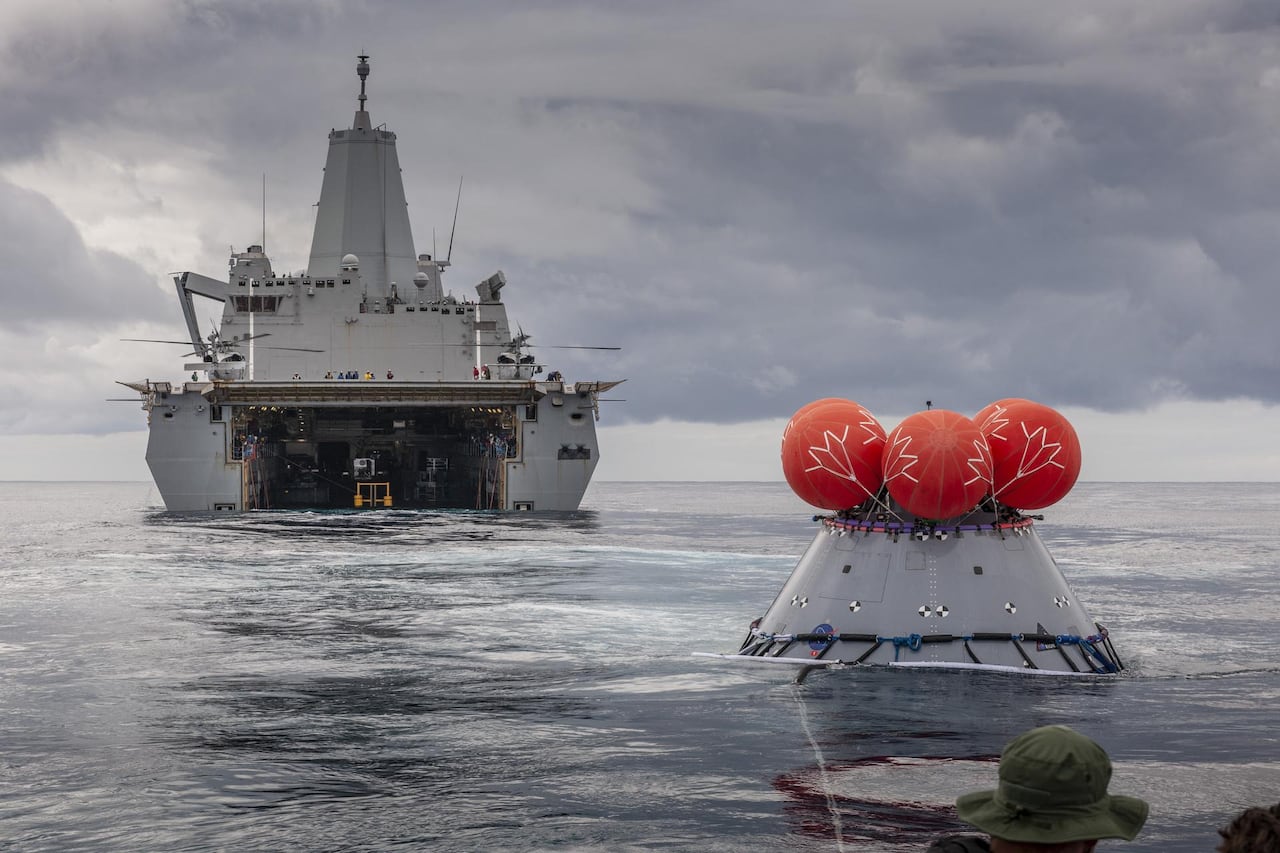 A space capsule with inflated balloons is seen in front of a ship.