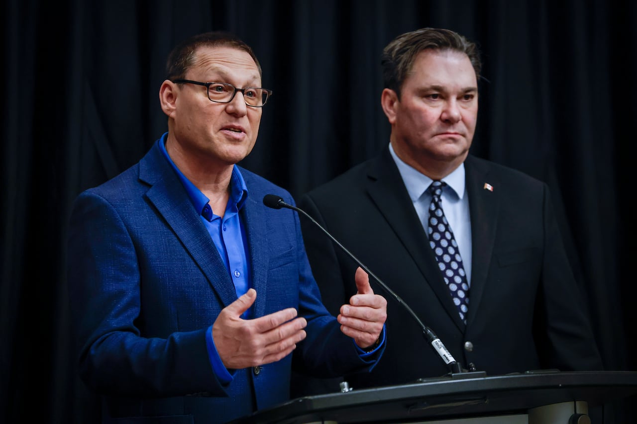 Don Davies looks at Avi Lewis speaking at a podium in Winnipeg.