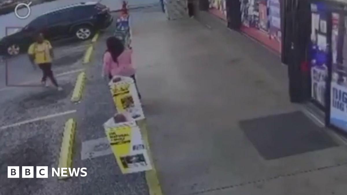 David Robinson is photographed indoors against a pale wall with a subtle floral pattern. He is shown from the shoulders up, wearing a light shirt and a dark jacket. The lighting is soft and even, and the background is uncluttered.