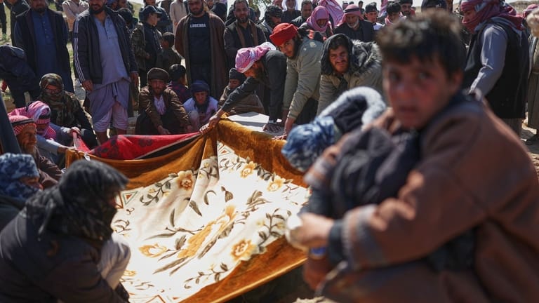Mourners cover a grave with cloth during the burial of...