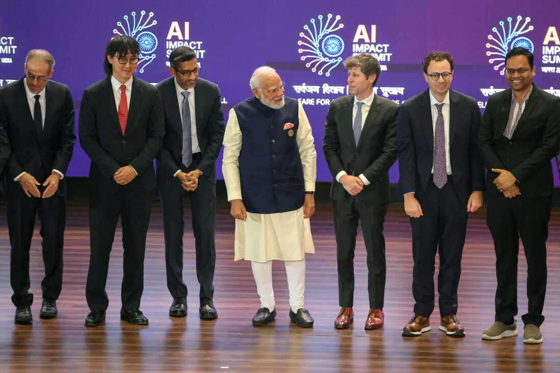 Indian Prime Minister Narendra Modi stands in the center of a row with six other men at the AI Impact Summit in New Delhi on February 19. The other men include OpenAI CEO Sam Altman (third from right), Anthropic CEO Dario Amodei (second from right), Google CEO Sundar Pichai (third from left) and Meta Chief AI Officer Alexandr Wang (second from left).