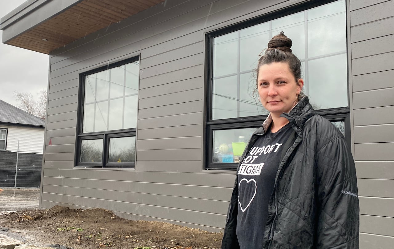A woman wearing a hoodie, jacket and with her hair in a bun has a serious look on her face. Her shirt reads "support, not stigma."