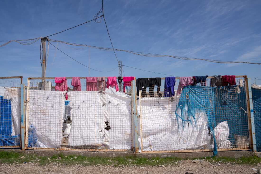 Pink and purple clothes hang on the top of a metal fence above tattered white and blue tents and tarps at Roj.