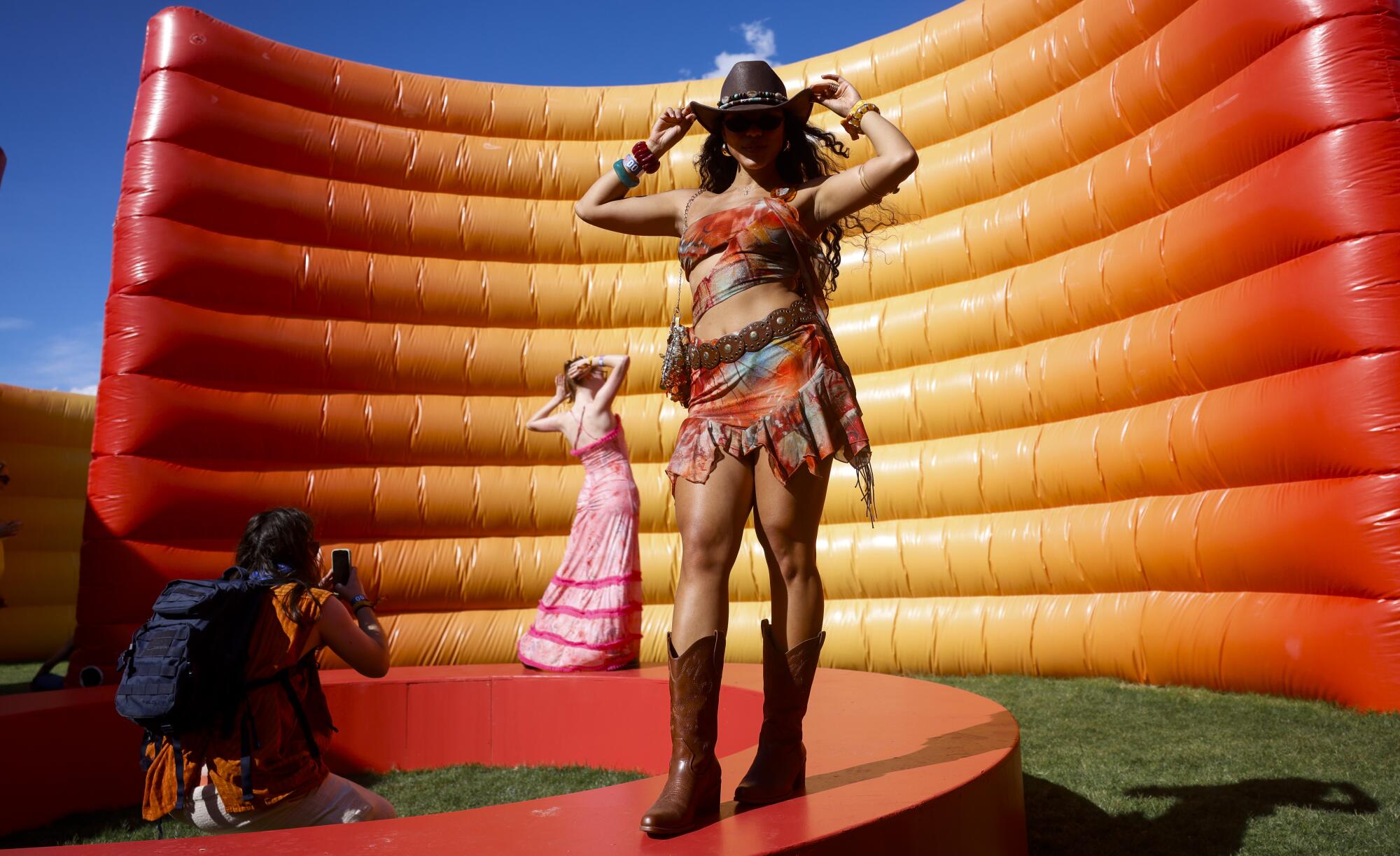Two women pose for a photographer in front of an orange-yellow curved wall that looks like a pool float standing on its side