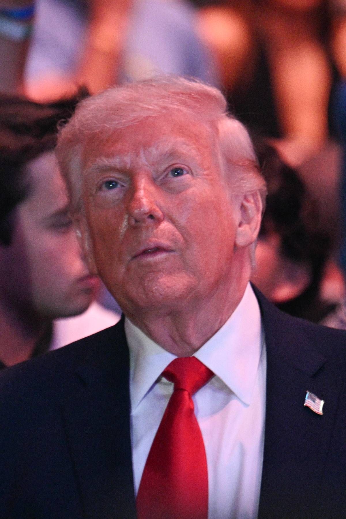 An individual, dressed formally, is intently focused on something in the foreground. Behind this individual, several other people are partially visible, suggesting a crowded or public setting.