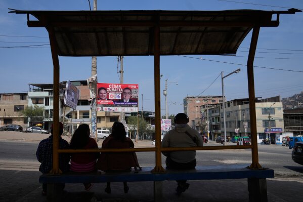 People sit in a bus station across the street from election campaign signs for presidential and congressional candidates, before the weekend's election in Lima, Peru, Friday, April 10, 2026. (AP Photo/Martin Mejia)