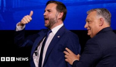 A man holds his thumb in the air while another man pushes him in the back from the right